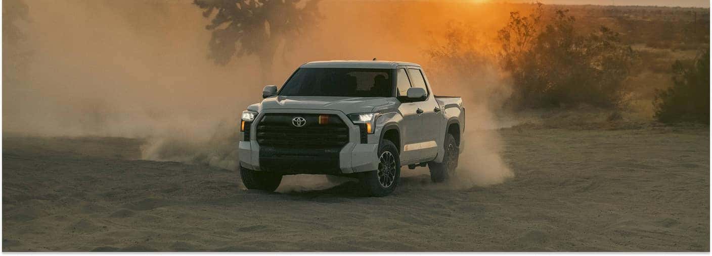 Front three-quarter view of a white 2026 Toyota Tundra kicking up sand on a desert trail.