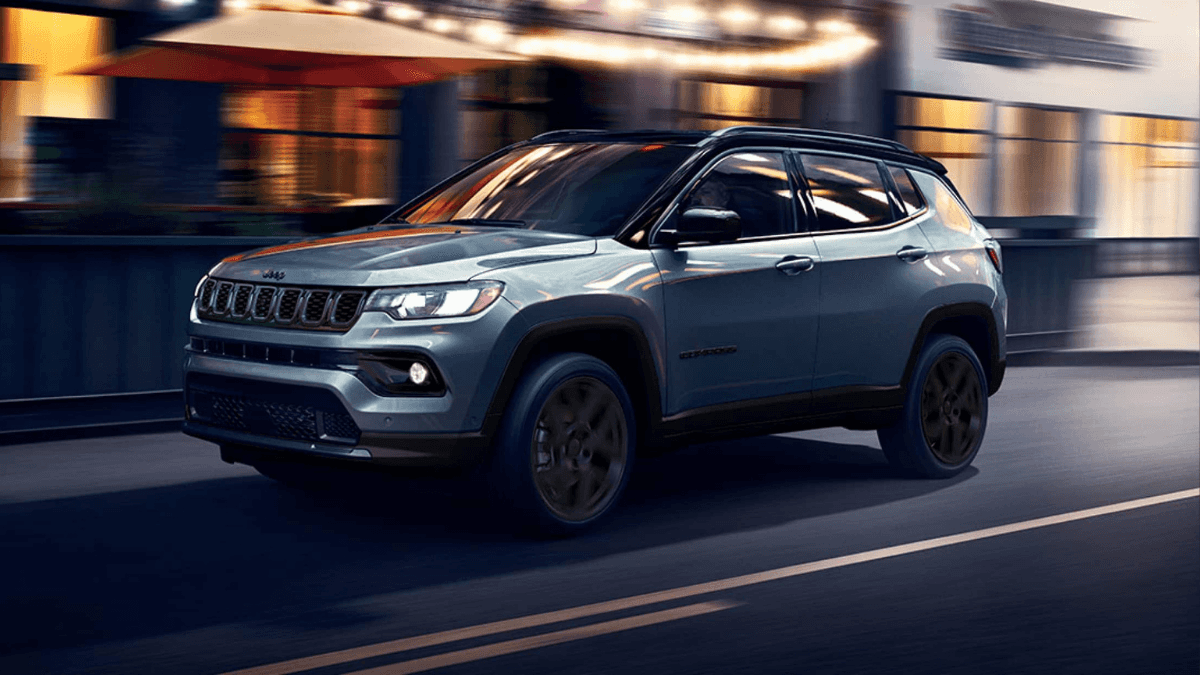 A light blue Jeep Compass driving through a city at night
