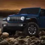 A blue Jeep Wrangler driving over rocks at sunset