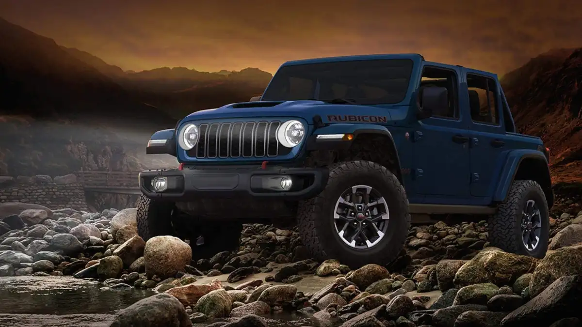 A blue Jeep Wrangler driving over rocks at sunset