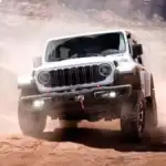 A white Jeep Wrangler kicking up dust as it drives off-road in a desert