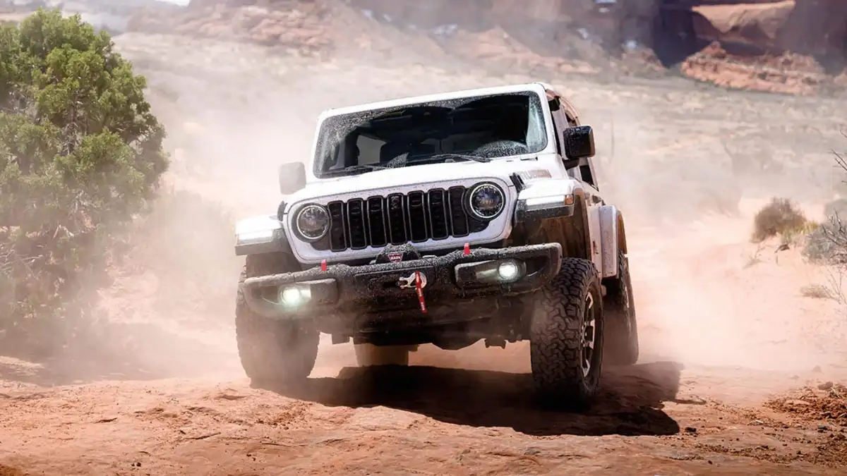 A white Jeep Wrangler kicking up dust as it drives off-road in a desert