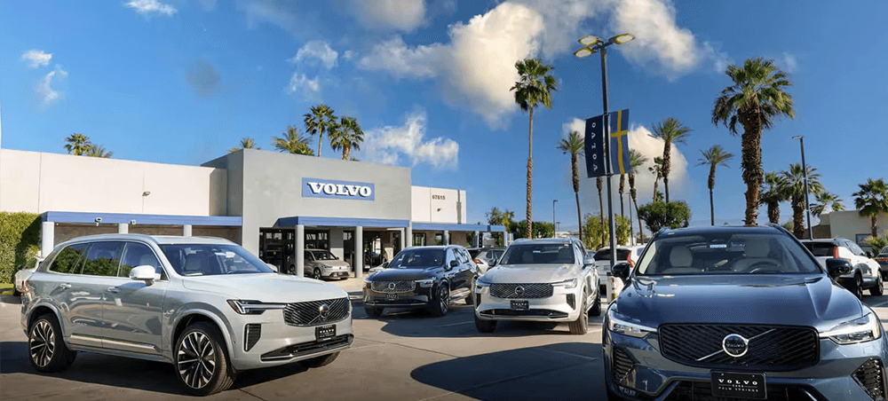 Front exterior of Volvo Cars Palm Springs dealership showcasing a white Volvo XC60 and a grey XC60 Recharge Plug-In Hybrid SUV.