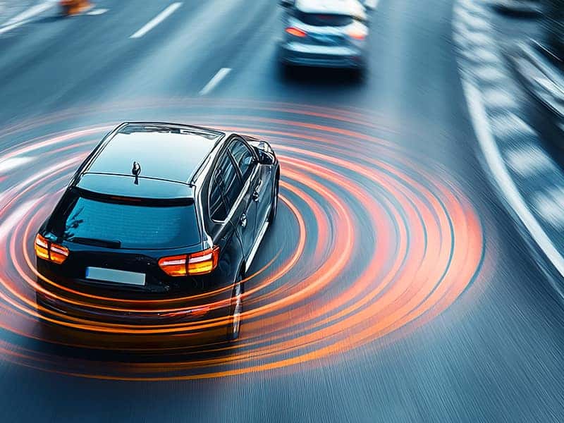Dark sedan with glowing brake lights photographed in motion on a highway, with orange and red light trails showing braking action.
