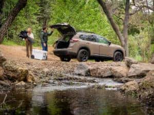 2025 Nissan Rogue Rock Creek edition parked next to a creek with two people unloading camping supplies